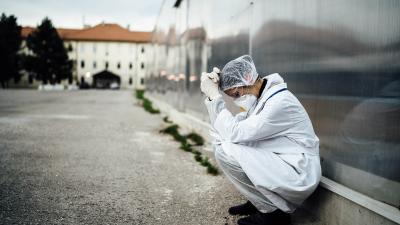 A woman in full personal protective equipment , she is seen kneeling down against a wall.